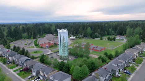 Orbiting-aerial-shot-around-a-suburban-water-tower-with-an-elementary-school-in-the-background