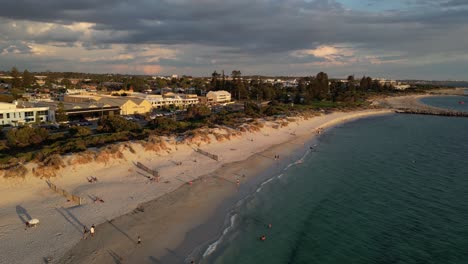 Drone-flight-over-sandy-south-beach-in-Fremantle-during-golden-sunset-time,-Western-Australia---Tourist-resting-and-enjoying-good-weather