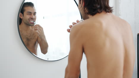 hombre cepillándose los dientes en el espejo del baño