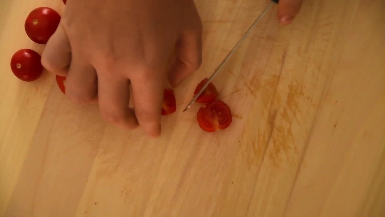 mano femenina cortando tomates pequeños y jugosos en una tabla de cortar de madera ligera con un cuchillo