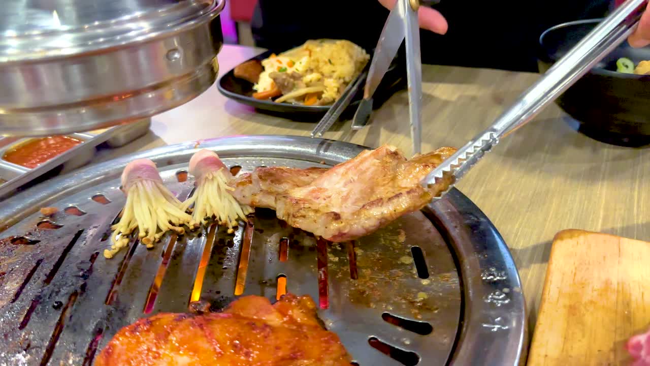Grilled meat and mushrooms on a Korean BBQ grill in a Bangkok restaurant. Bright lighting highlights the vibrant colors and sizzling action
