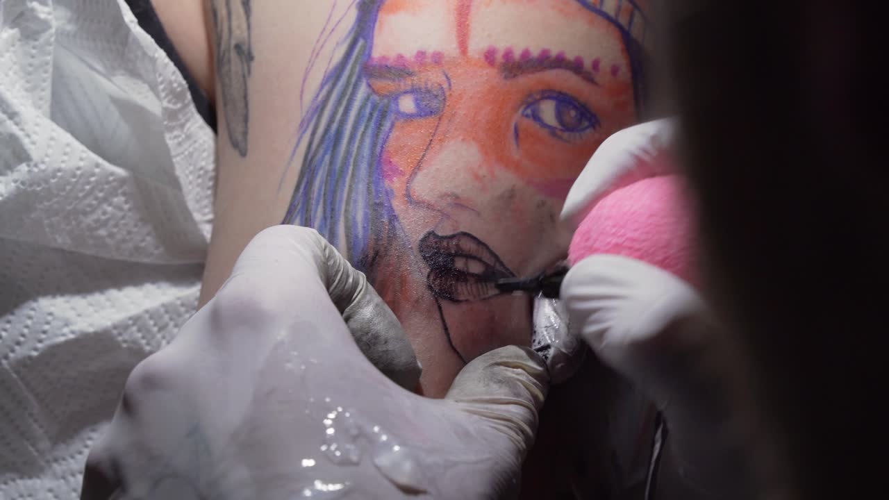 primer plano de un artista del tatuaje haciendo un tatuaje en el brazo de un joven en el salón, tatuando los labios de la cara de la chica