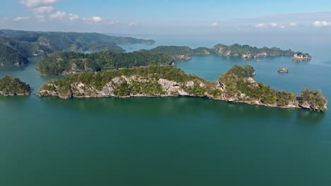 breathtaking drone shot showing rocky islands in ocean covered with plants during sunny day - tourist boats arriving during trip -