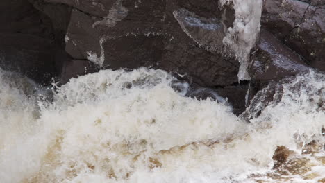 Nahaufnahme-Von-Wasser-Aus-Der-Frühlingsschneeschmelze,-Das-Gegen-Eisige-Felsen-Prallt