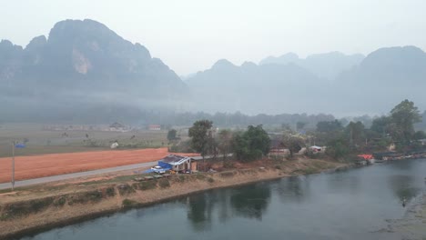 drone-shot-of-river-with-mountains-in-the-distance-in-Vang-Vieng,-the-adventure-capital-of-Laos