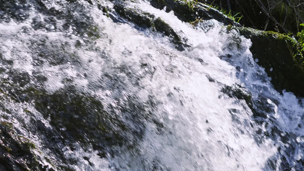 Slow Motion Waterfall Cascading Down Over Mossy Rocks with Bright Sunshine in Wales. Fast Moving Water in Natural Countryside.