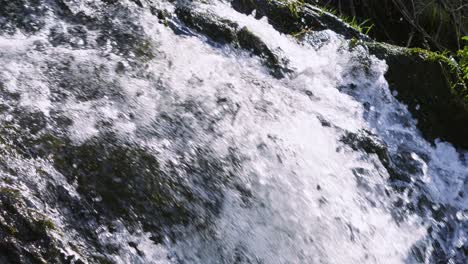 slow motion waterfall cascading down over mossy rocks with bright sunshine in wales. fast moving water in natural countryside.
