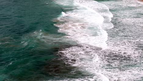 Aerial-view-of-a-wave-breaking-on-a-golden-sandy-beach,-The-mesmerizing-patterns-of-foam-and-surf