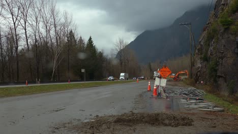 equipo de construcción, conos naranjas y señales de tráfico al lado de la carretera, durante la lluvia