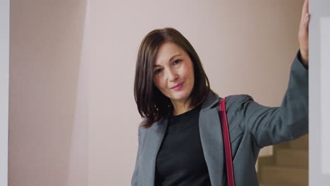 businesswoman smiling confidently while holding bag in office corridor, modern workspace with neutral colors, professional woman in business attire looking at camera