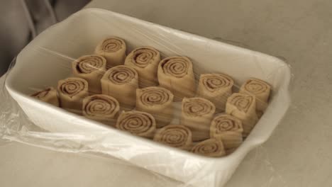 chef caucásico cubriendo rollos de canela caseros en una bandeja de horneado de cerámica