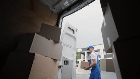 two young workers of removal company unload boxes and furniture from minibus into customer's home