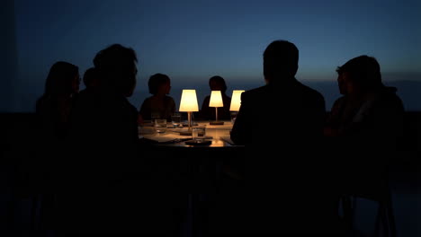 group of people in silhouette around a table in dim light at night