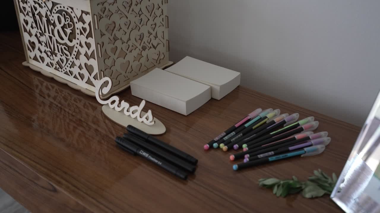 Wedding card station with a decorative box, markers, and pastel pens on a wooden table