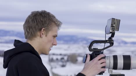 nature videographer in snowy landscape, decked out filming rig with monitor, 4k