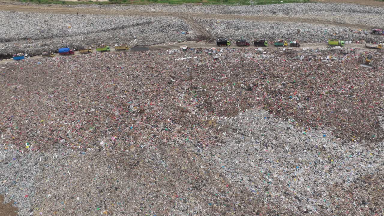 Aerial view of large landfill with garbage trucks unloading waste