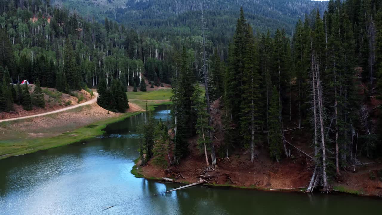 hermoso dron aéreo de camiones izquierdo tomado de un impresionante paisaje natural del lago del embalse del prado anderson hasta el cañón del castor en utah con un gran bosque de pinos, un pequeño arroyo y un campo de hierba