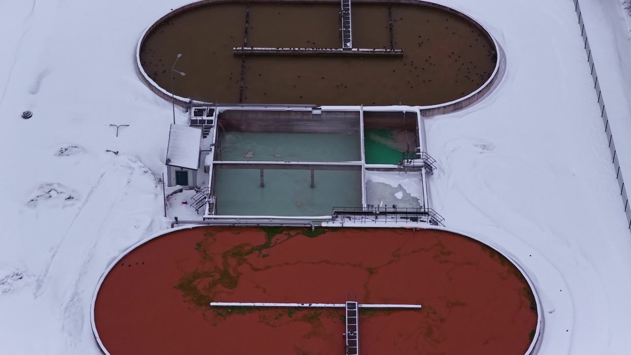 Sewage treatment facility with large sedimentation tanks in winter in aerial view