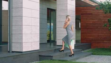 elegant woman talking mobile near luxury house. beautiful woman going with bags