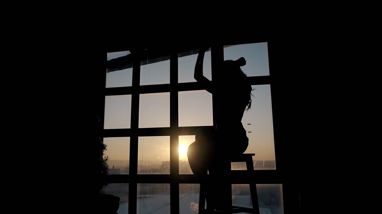 woman enjoys music and dances on stool at window in evening