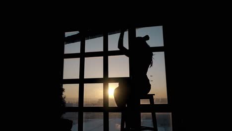 woman-enjoys-music-and-dances-on-stool-at-window-in-evening