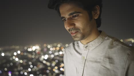 a young indian asian man is sitting outdoors and using mobile phone