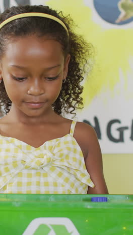 video of happy african american girl holding box with recycling symbol in classroom