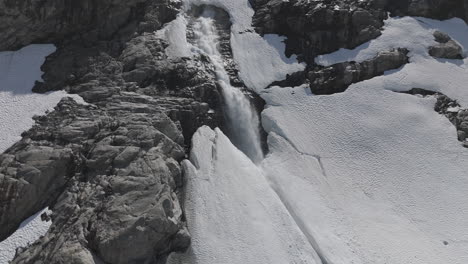 slowmotion drone shot flying around a powerfull waterfall near langvatnet lake in norway close to the strynefjellsveg breaking through ice and snow on a sunny day surrounded by shiny rocks log