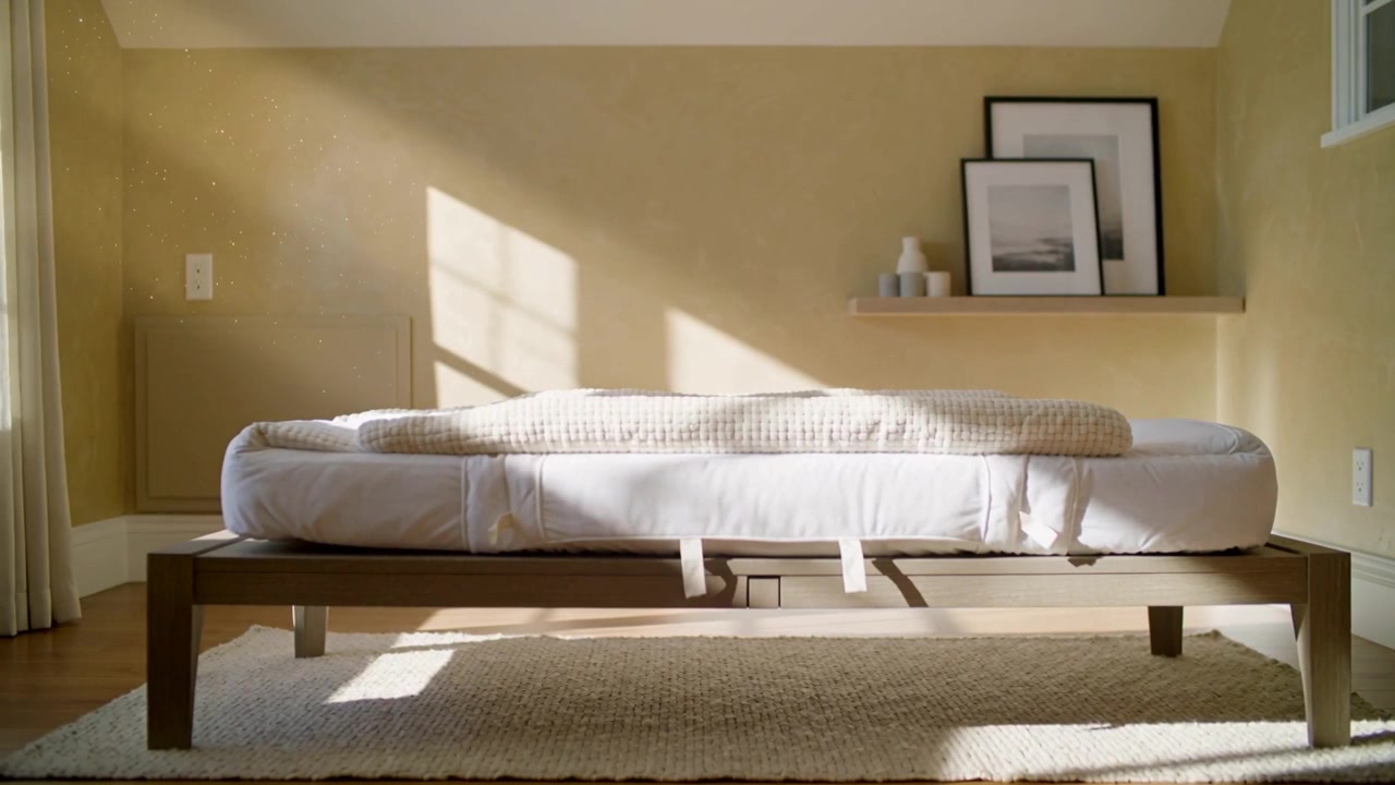 Luce solare che si sposta attraverso la finestra, muovendosi su un letto a piattaforma con una coperta beige piegata in camera da letto.