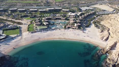 aerial view of a beautiful beach with hotel buildings and blue sea with swimming sailing boats and majestic cliffs at santa maria beach in cabo san lucas during a beautiful vacation