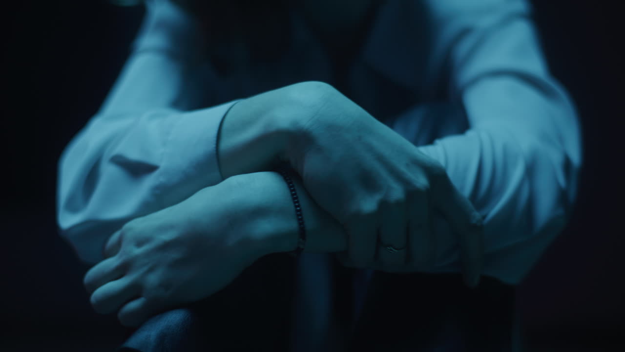 Close-up of a woman sitting with her hands on her knees in a dimly lit room
