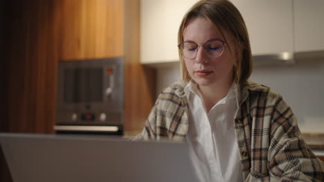 mature businesswoman working from home focused woman is working with her laptop and paper documents sitting in the kitchen at home. laptop app calculate costs expenses estimate budget for project