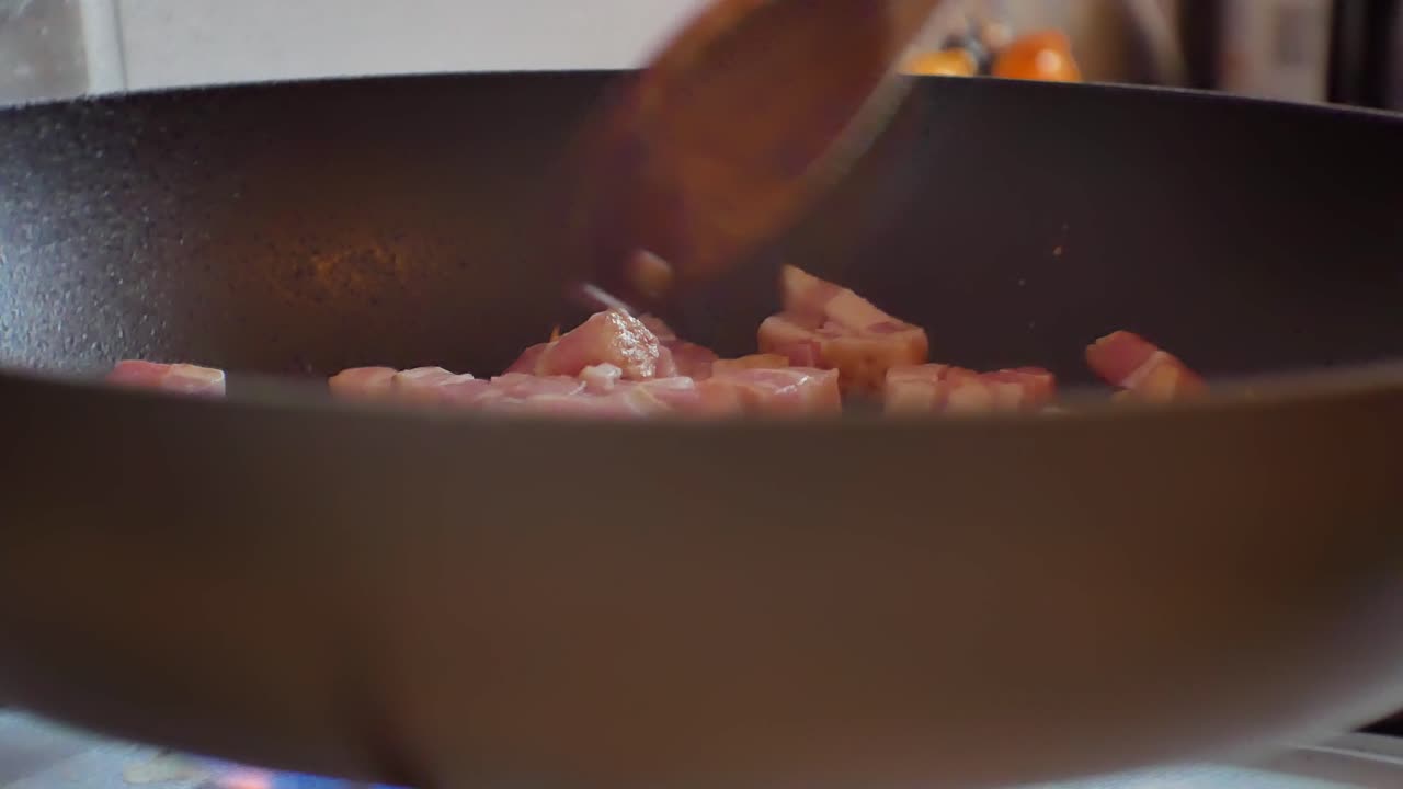 Close up shallow focus on fresh chopped bacon pieces in hot steaming frying pan on cooker stove
