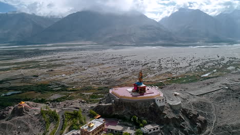 aerial dolly shot of a distant lord budha statue situated in the middle of a high altitude mountain valley