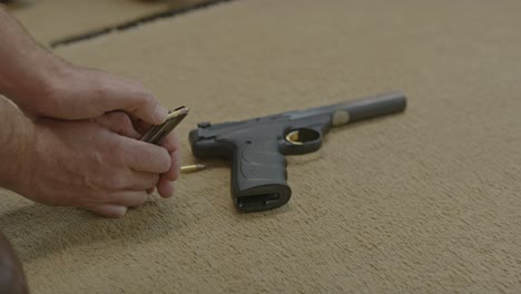 hombre descargando balas de un cargador de pistola mientras una pistola de pequeño calibre está tendida en un banco
