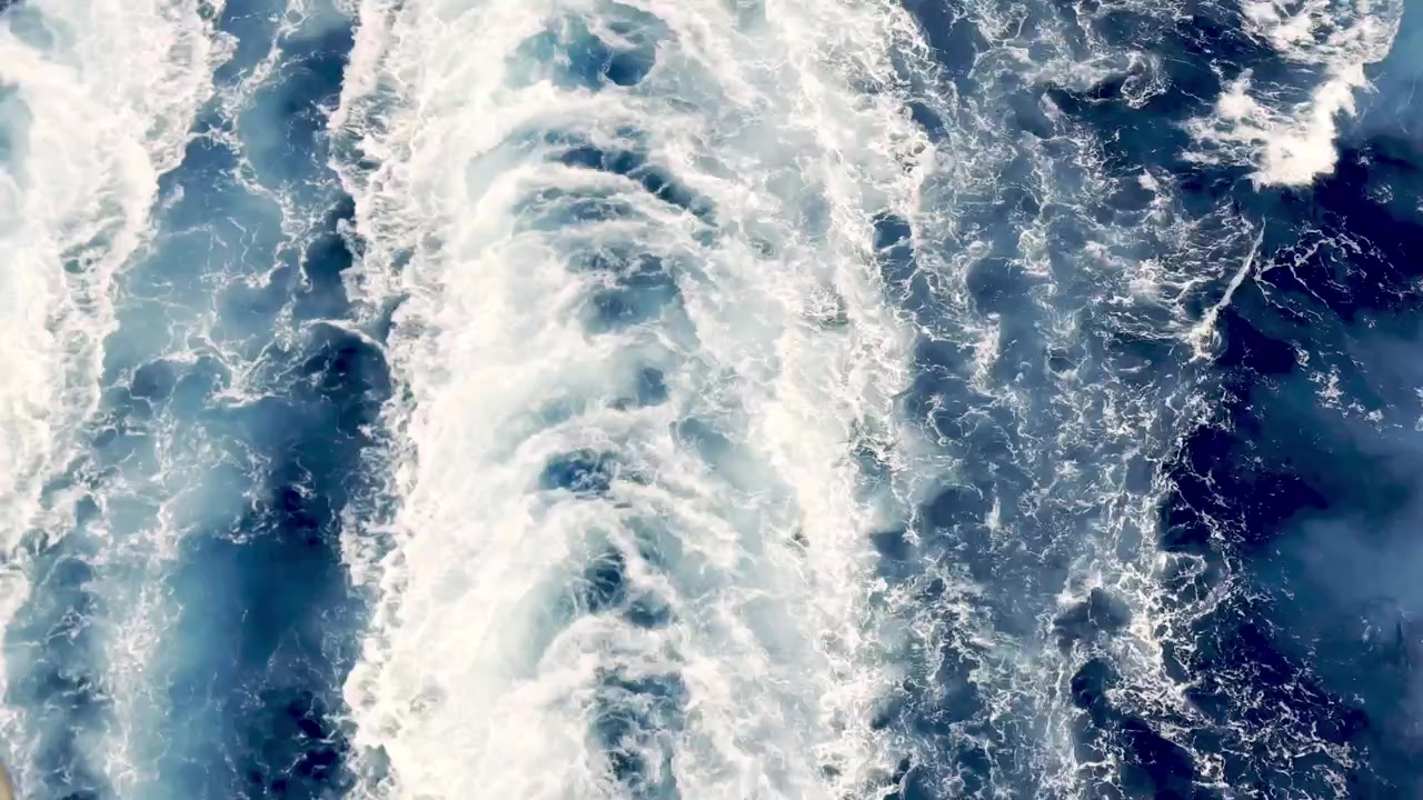 Schäumende weiße Heckwelle pflügt durch tiefblaues karibisches Wasser hinter einem fahrenden Kreuzfahrtschiff