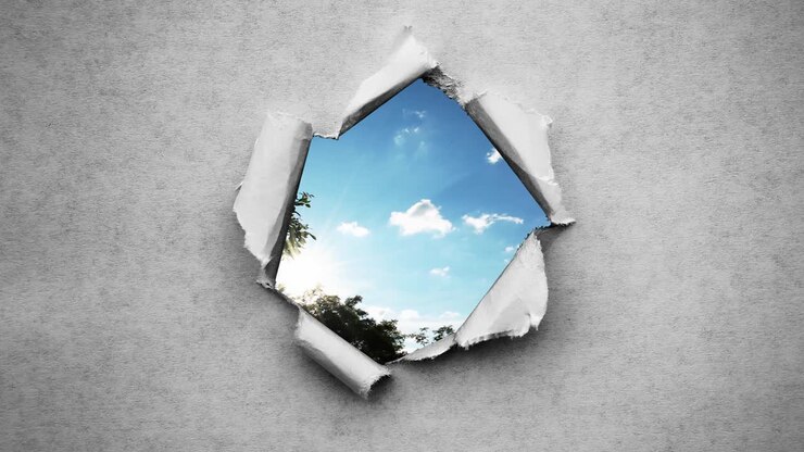 Creative 4k time laps video of fast moving clouds in the blue sky that are visible through a circle hole with torn edges in old retro grunge vintage paper.