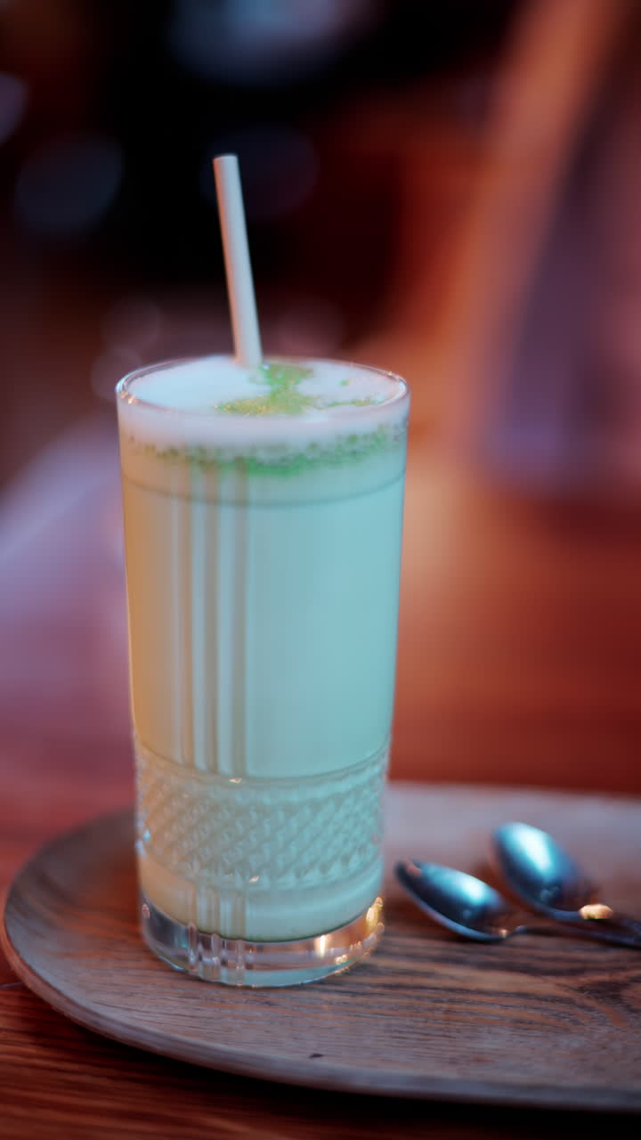 Close up of a matcha latte in a glass with a straw on a table at a cafe. Vertical