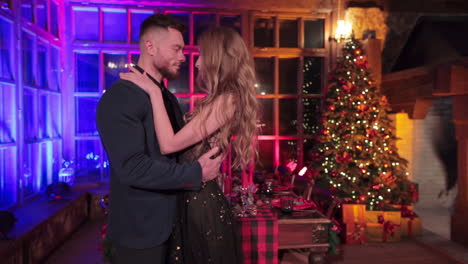 passionate dating couple in festive clothes hug standing in the decorated room. beautiful young people near the served table for christmas dinner.