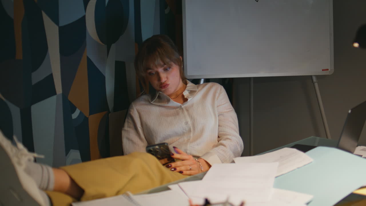 Relaxed boss texting smartphone at night cabinet. Employee putting legs on table