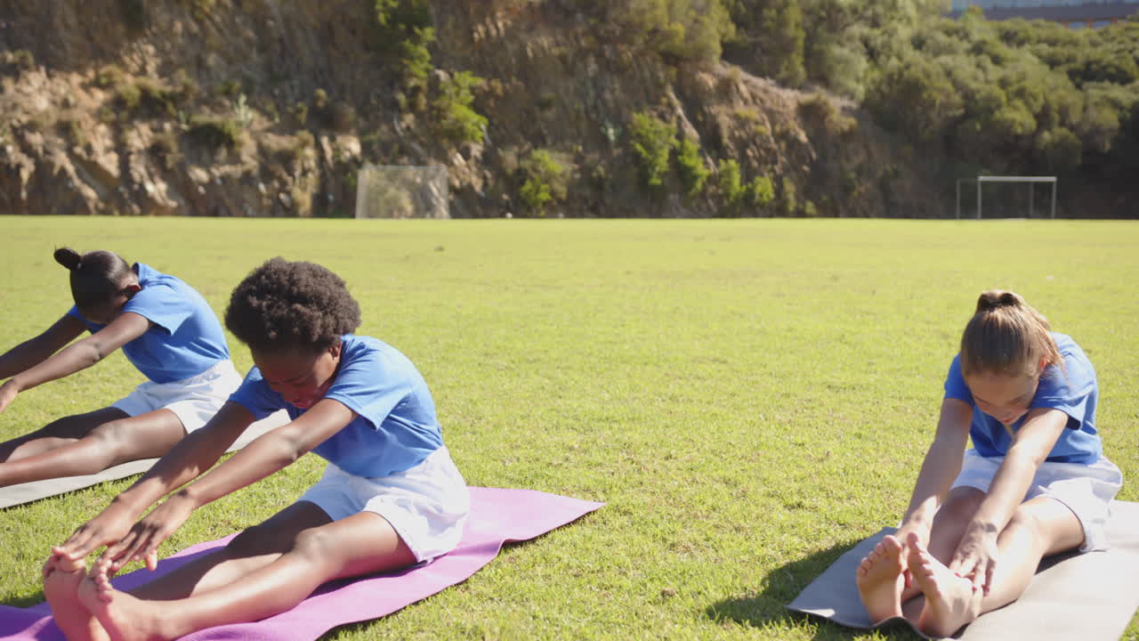 Stretching on yoga mats, girls exercising outdoors in school physical education class