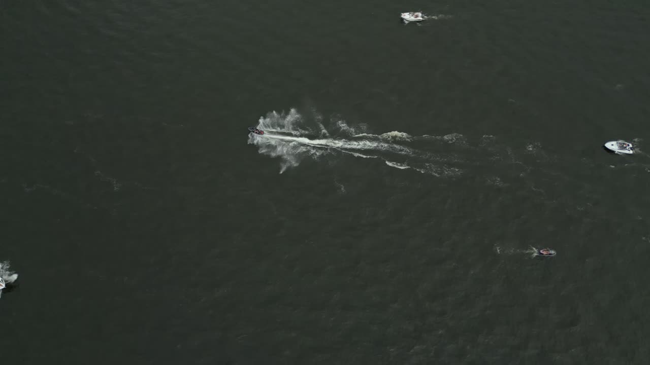 Boats speeding through open water leaving white trails against the dark green surface