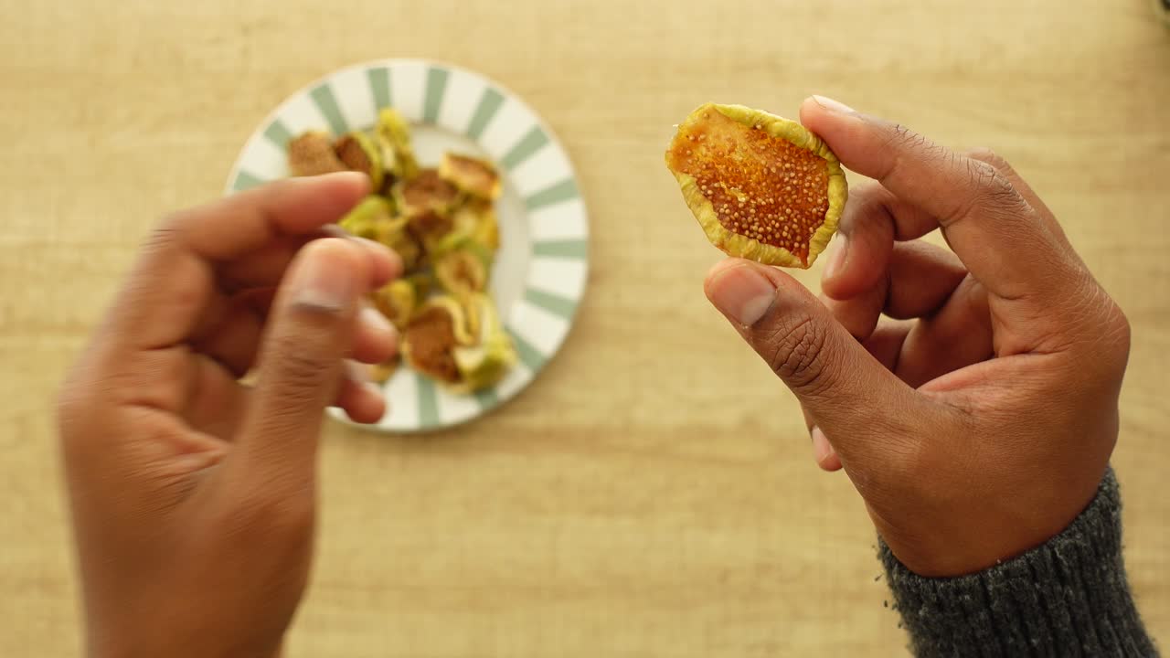 Hands holding and examining dried figs with a plate of figs in the background