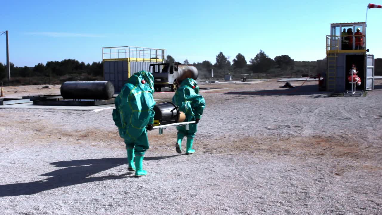 들것을 산업 지역으로 운반하는 방호복을 입은 두 사람