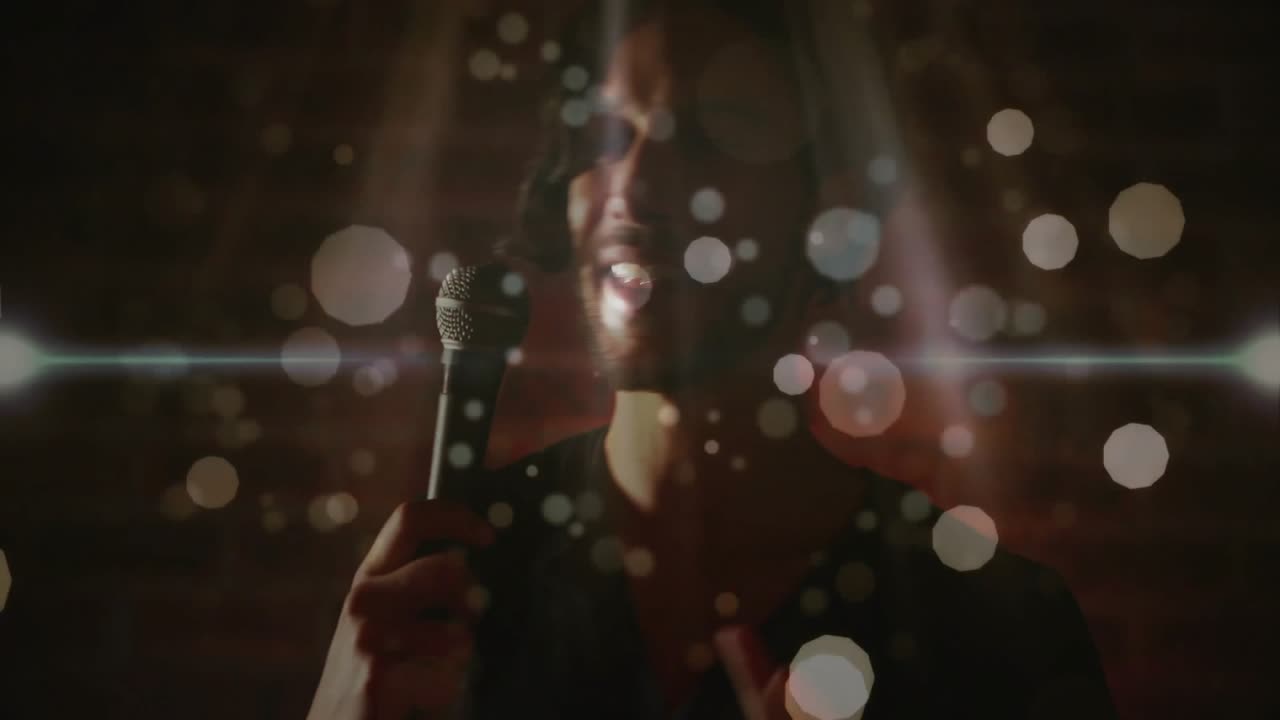 Sanger løfter mikrofonen til munden og slipper en tone løs under en musikoptræden mod en murstensvæg med bokeh.