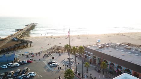 american flag flutters in square in front of beach and wooden pier