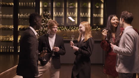 group of friends wearing elegant clothes talking while they holding champagne glasses in new year's party