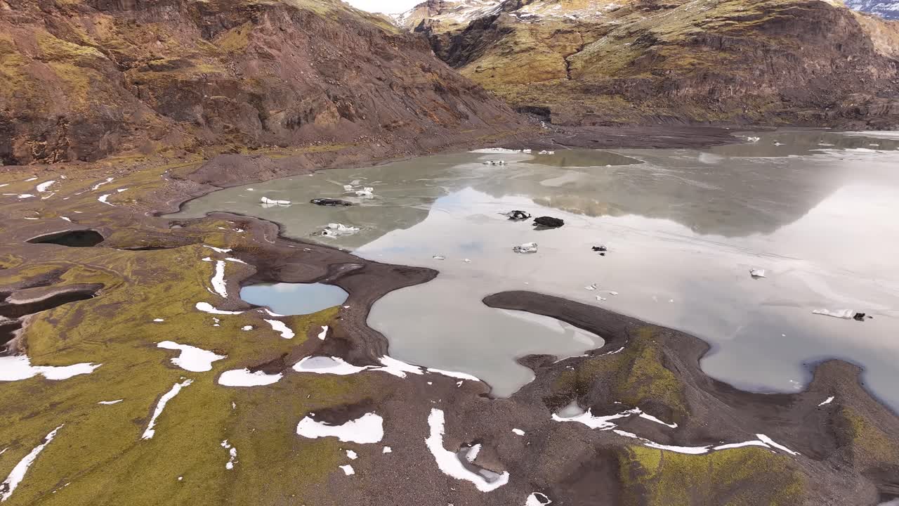 Aerial view of the glacial tongue of Sólheimajökull, Iceland, meeting a milky glacial lagoon. Rugged landscape showing ice formations and meltwater.