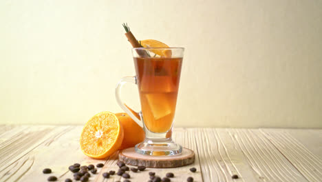 a glass of iced americano black coffee and layer of orange and lemon juice decorated with rosemary and cinnamon