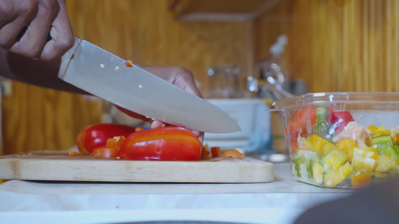 una toma estática en cámara lenta de un hombre negro en la cocina, cortando pimientos rojos cerca de un fregadero